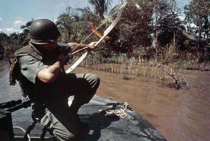 le lieutenant commandant donald d. sheppard, de coronado, en californie, pointe une flèche enflammée sur une hutte en bambou dissimulant un bunker viet cong fortifié sur les rives de la rivière bassac, au vietnam, le 8 décembre 1967.