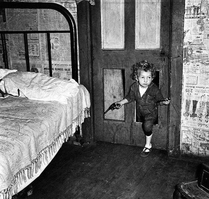 l’enfant d’un mineur de charbon utilise un trou dans la porte pour entrer dans une chambre avec une pipe dans une main et un pistolet dans l’autre à bertha hill, virginie occidentale. photo de marion post wolcott. 1938