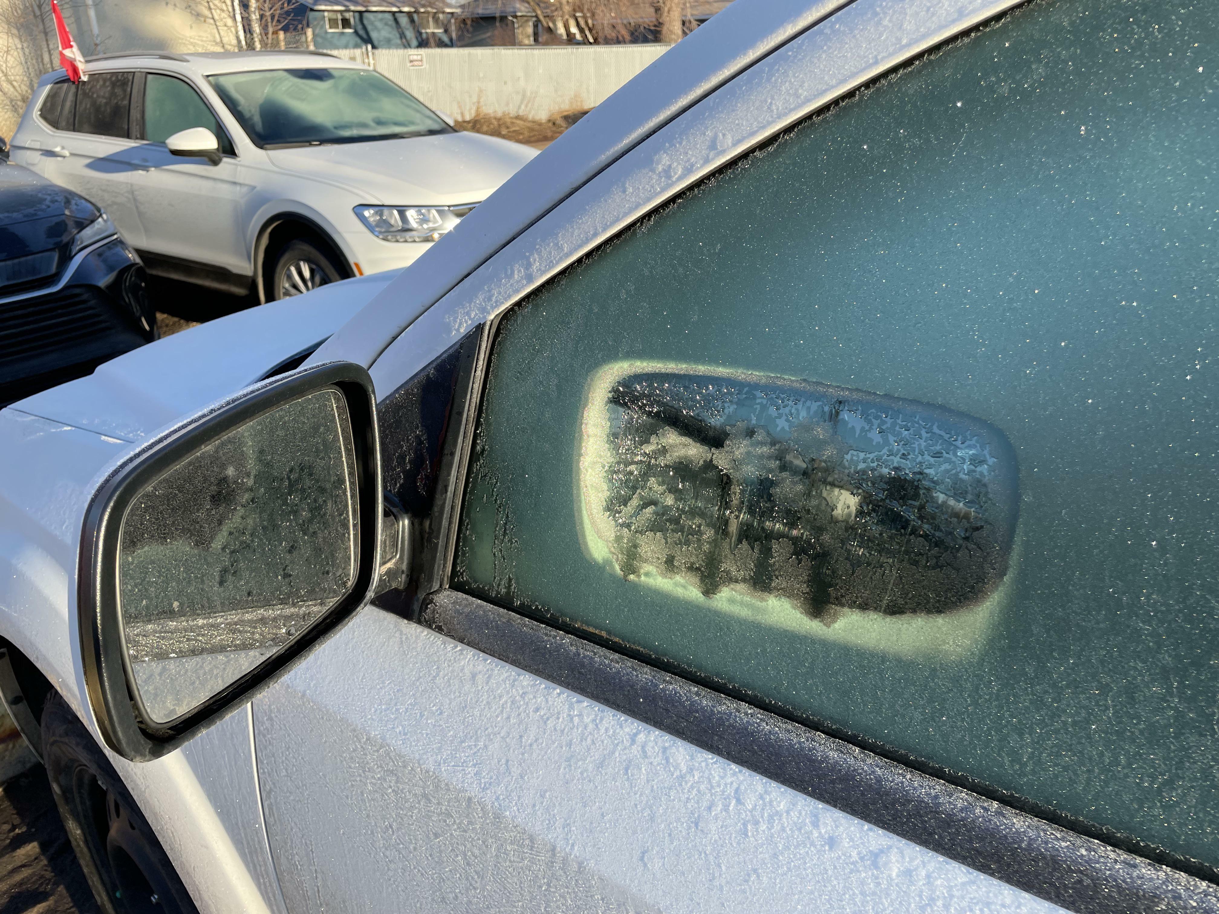 Le soleil qui se reflète sur mon rétroviseur latéral a fait fondre un trou en forme de miroir dans le givre de la fenêtre.