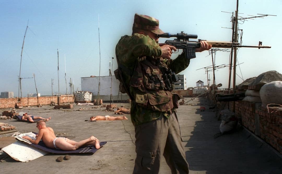 Russian Soldiers Sunbathe On A Rooftop While A Sniper Stands Guard In Grozny, Chechnya, 9 May, 2000