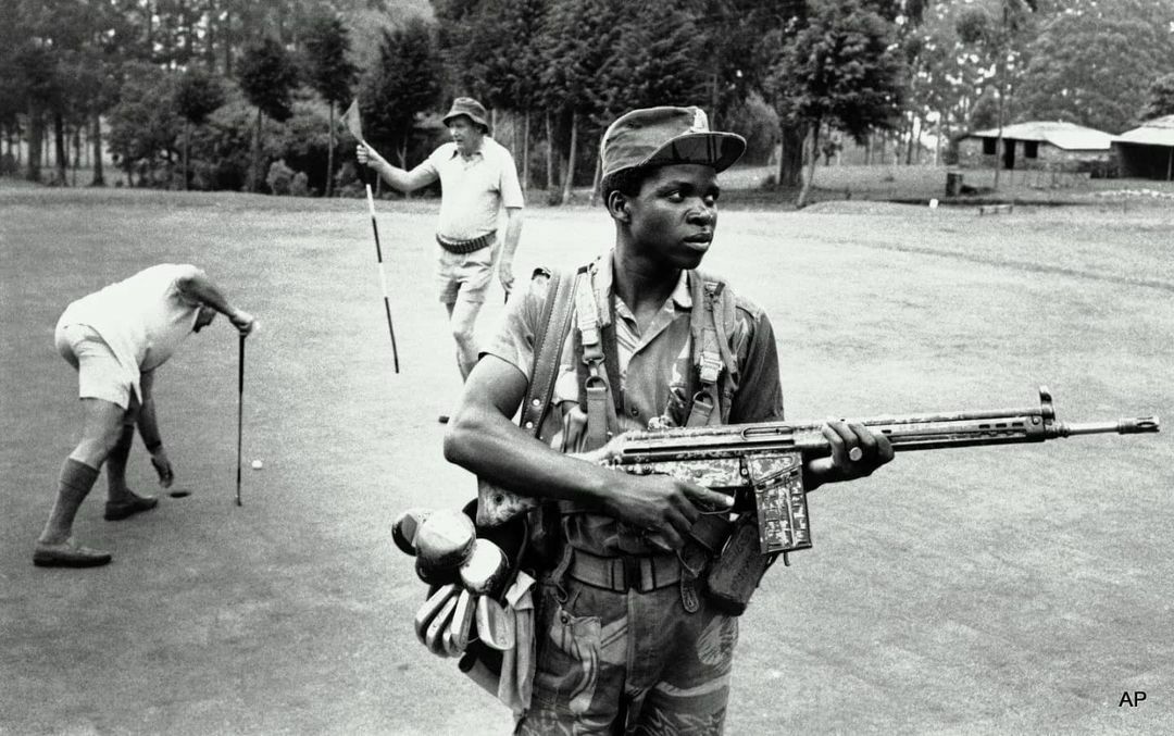 An Armed Guard Provides Both Service And Security To White Golfers At A Golf Course At The Hotel Leopard In Rhodesia, 1978