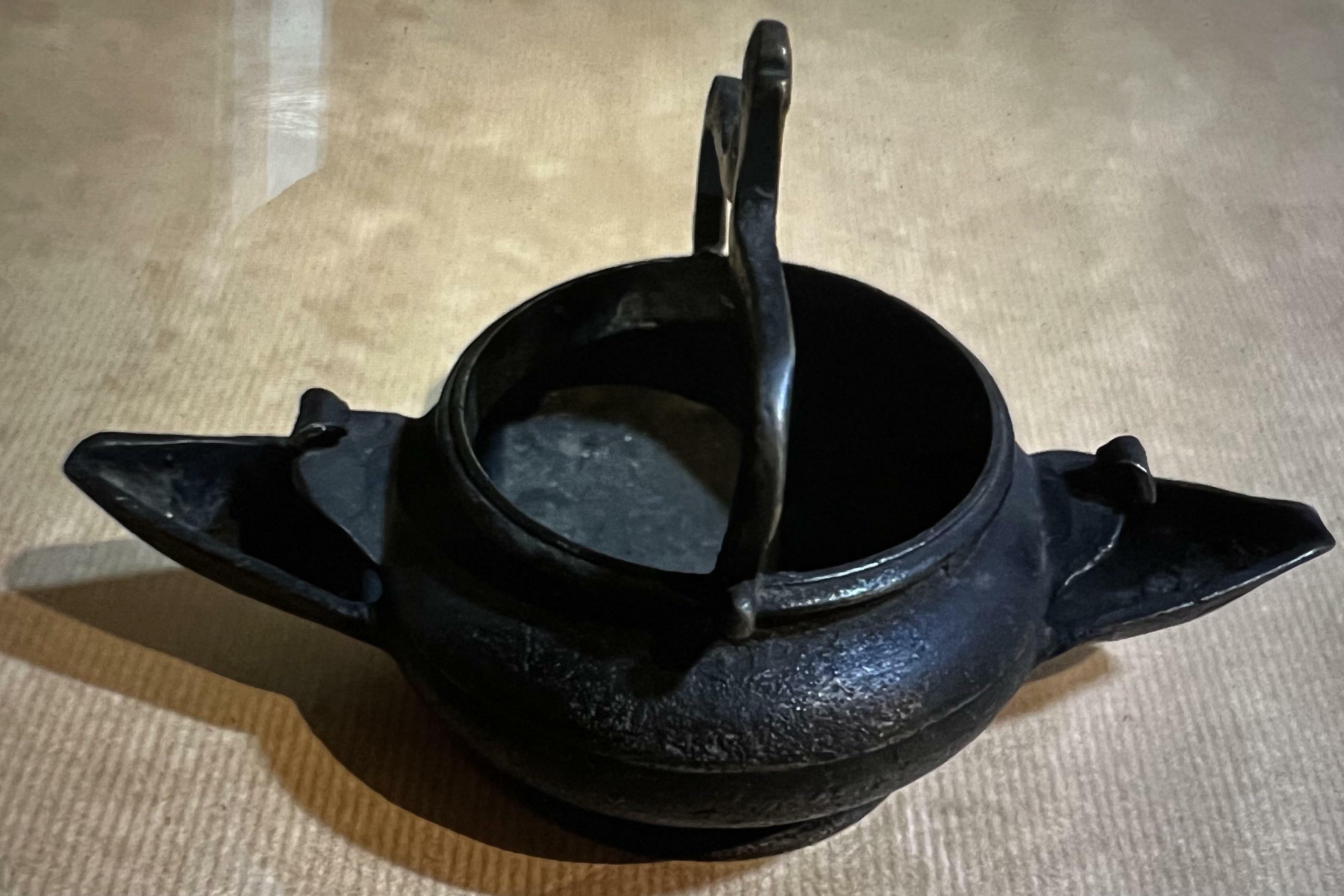Quel est cet ancien pot en bronze à deux becs qui ressemble à un lavabo suspendu mais dont le col est trop bas pour transporter de l'eau sans la renverser ?