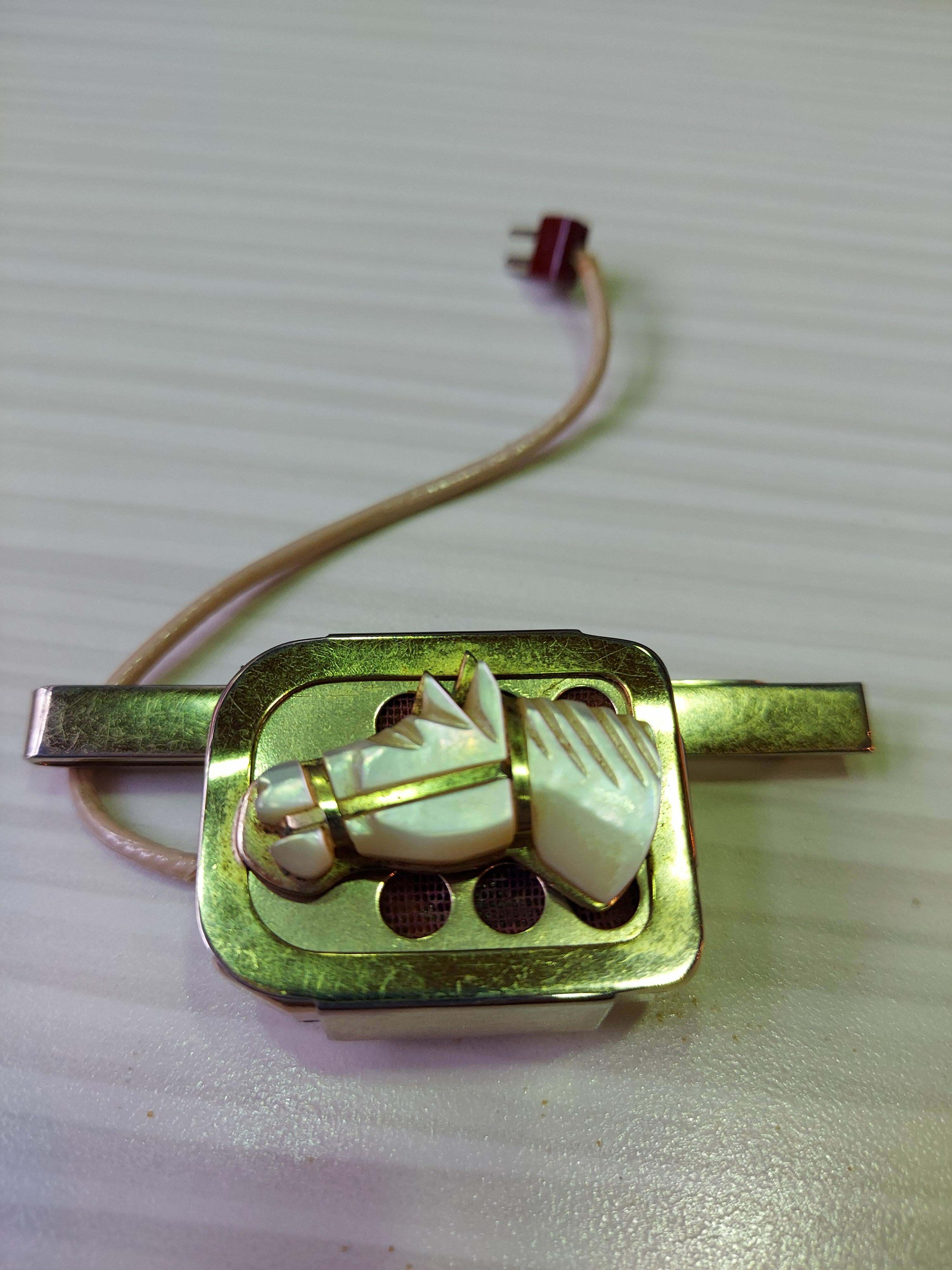 C'est un haut-parleur plaqué or avec un court cordon à deux broches à l'extrémité, il y a aussi un clip plaqué or avec une opale représentant un cheval dessus.
