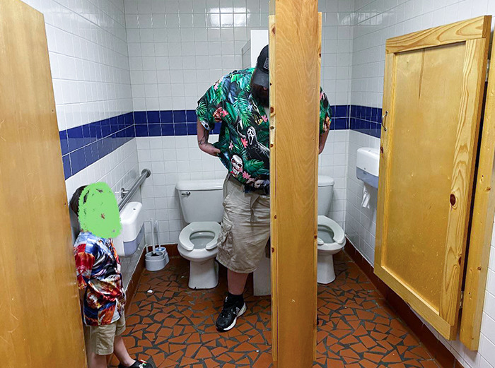 Salle de bains d’une pizzeria. 2 toilettes sont séparées par un mur qui n’atteint pas les portes. L’endroit où se tient mon conjoint est juste un espace où tu peux avoir un voisin de salle de bain.